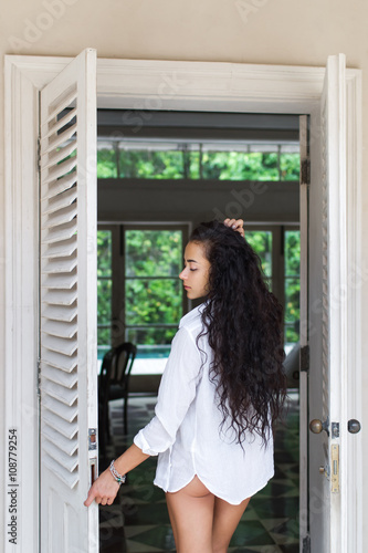 Beautiful woman with long black hair posing near white door in b