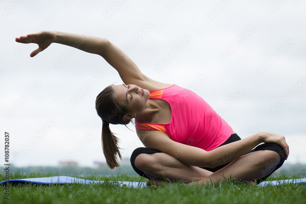 Fototapeta premium Young woman doing stretching exercises at open air
