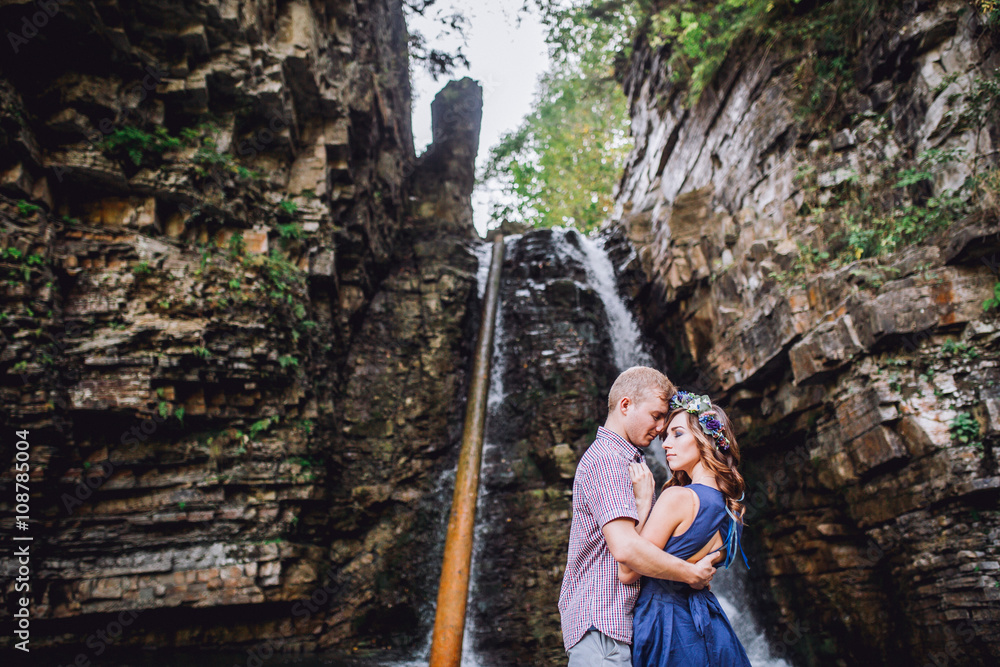 Portrait of a young couple is hugging each other near a waterfall