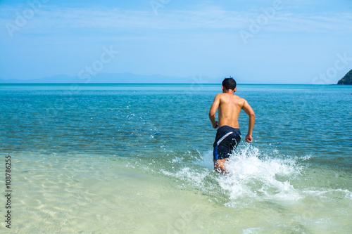 Man without shirt running into the sea water near the beach