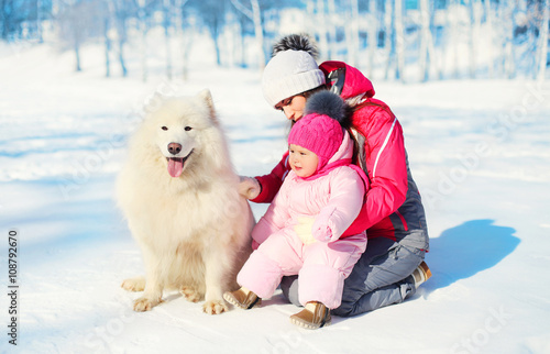 Mother and baby with white Samoyed dog together on snow in winte