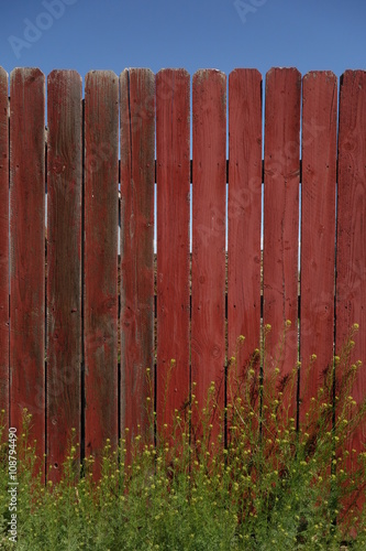 Rustic Red Fence with Green Plants and Blue Sky