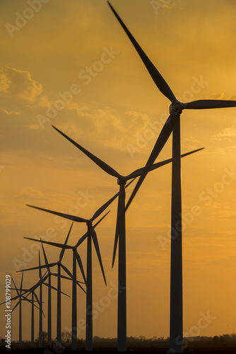 Windmill wind turbine generating power turning silhouetted against sunset sky