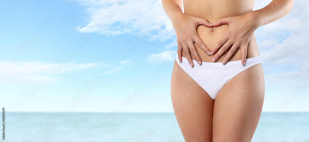 woman hands heart shape on belly, isolated on summer sea and sky