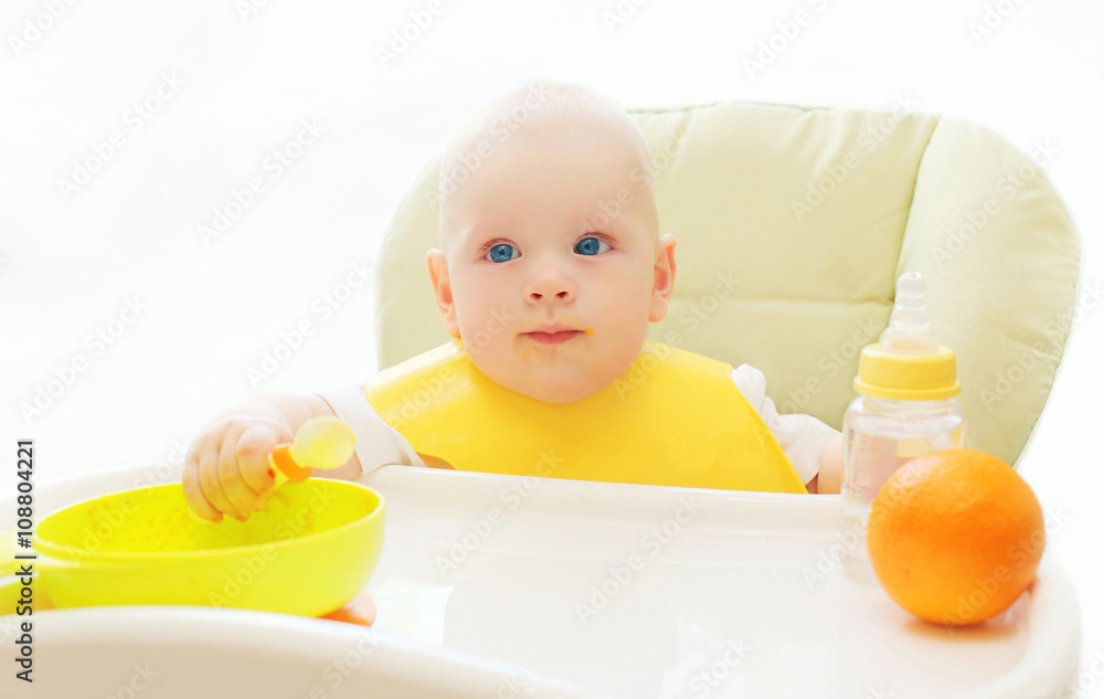 Baby sitting at the table home and eats spoon Baby sitting at the table home and eats spoon