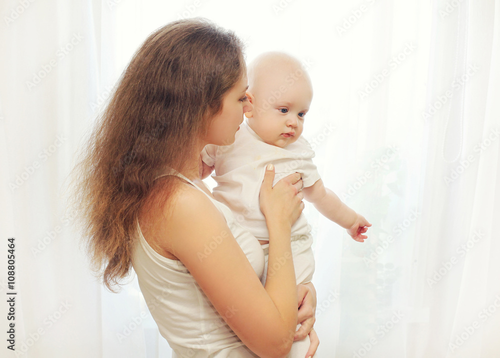 Portrait mother hugging her baby over white window Portrait mother hugging her baby over white window