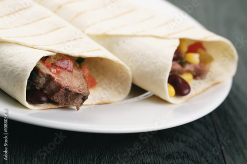 burritos with beef steak, corn, black beans and salsa sauce on wood table