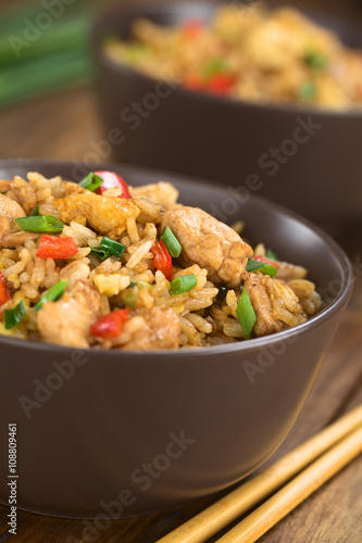Homemade Chinese fried rice with vegetables, chicken and fried eggs served in brown bowl with chopsticks on the side (Selective Focus, Focus on the top of the dish)
