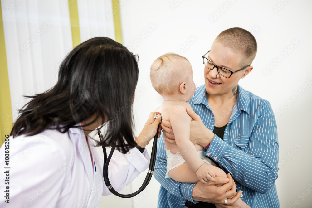 Female Pediatrician Examining Baby Carried By Mother Female Pediatrician Examining Baby Carried By Mother
