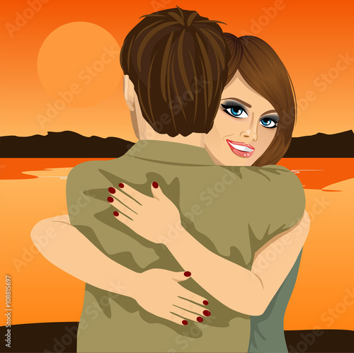 Young couple hugging on bank of river in evening at sunset