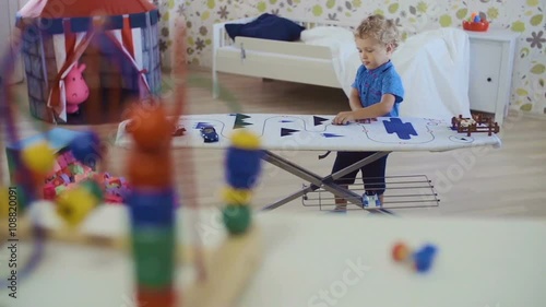 Little curly-headed boy playing with toys in room
