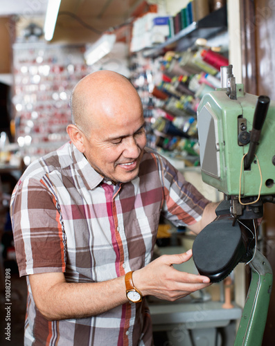 Mature workman sewing leather boots on stitch lathe