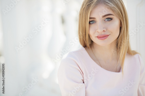 Beautiful woman with long blonde straight hair and grey eyes,light makeup,dressed in a pink t-shirt ,spends time alone on a city street,posing for the photographer,smiling sweetly
