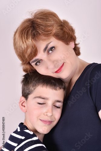 Mother and son with head to head smiling and hugging each other. Son with his eyes closed and mother looking at the camera. 