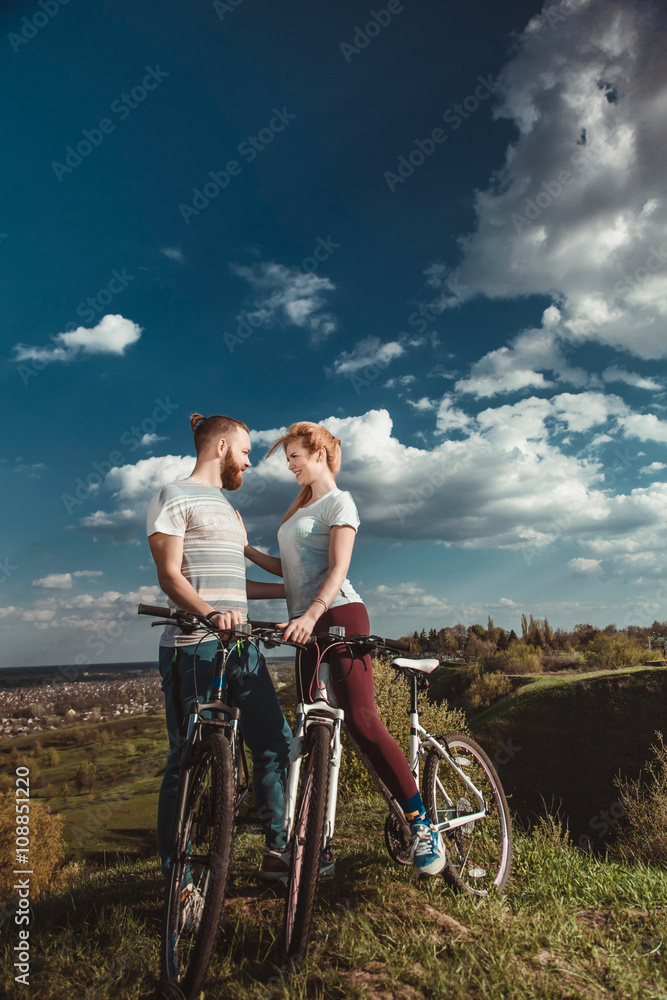 Beautiful young couple in love walking with bicycles hugging and looking at each other. The concept of joy and happiness