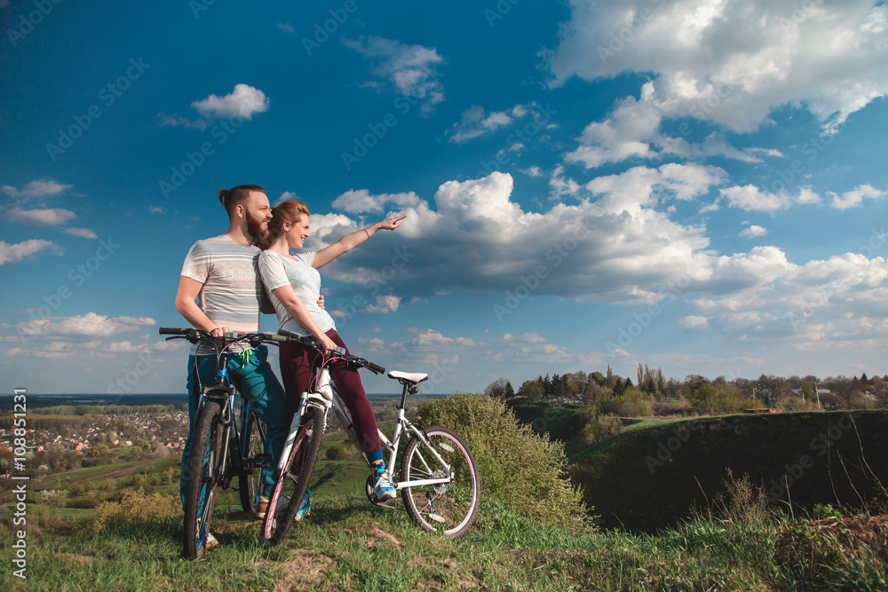 Beautiful young couple in love walking with bicycles, looking towards the beautiful nature and the blue sky. The concept of active rest Beautiful young couple in love walking with bicycles, looking towards the beautiful nature and the blue sky. The concept of active rest