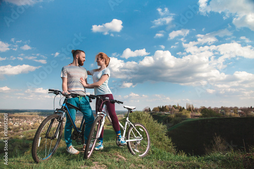 Fototapeta Naklejka Na Ścianę i Meble -  Beautiful young couple in love walking with bicycles hugging and looking at each other. The concept of joy and happiness