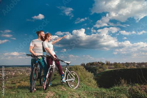 Fototapeta Naklejka Na Ścianę i Meble -  Beautiful young couple in love walking with bicycles, looking towards the beautiful nature and the blue sky. The concept of active rest
