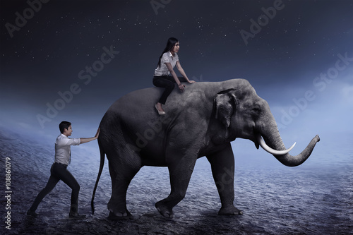 Business man help pushing elephant while his friend sit on it