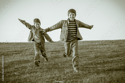 Two boys running together on meadow, sepia toned
