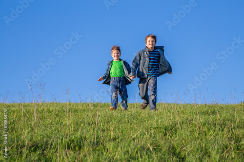 Two boys running together on green hill