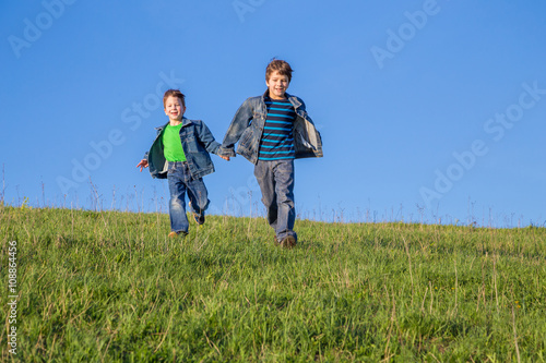 Two boys running together on green meadow