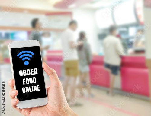 word order food online on smartphone in hand blurred waiting line up people at fast food restaurant, focus at smartphone