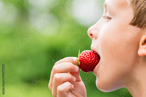 Boy eating fresh red strawberry
