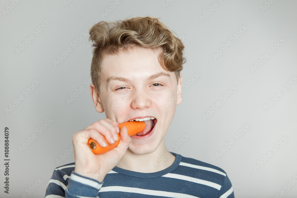 Young teenage boy biting a fresh raw carrot Young teenage boy biting a fresh raw carrot