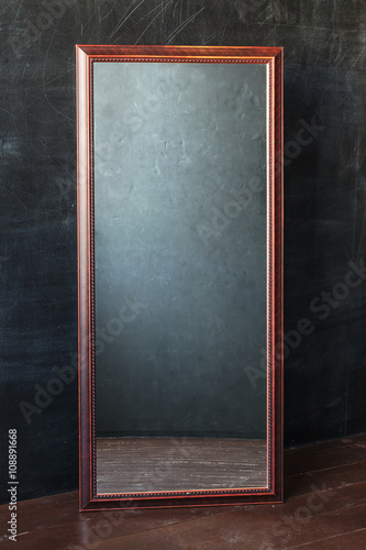 Classic rectangular mirror withot reflection standing In the empty room with black wall.
