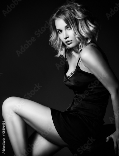 Sexy blond woman in black silk lingerie over dark background.