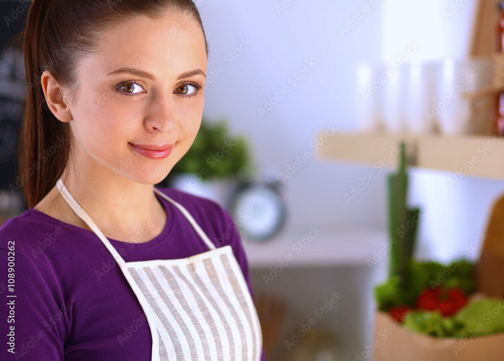 Young woman standing in her kitchen near desk with shopping bags Young woman standing in her kitchen near desk with shopping bags