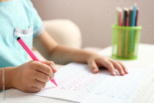 Schoolkid learns to write on sheet of paper, closeup