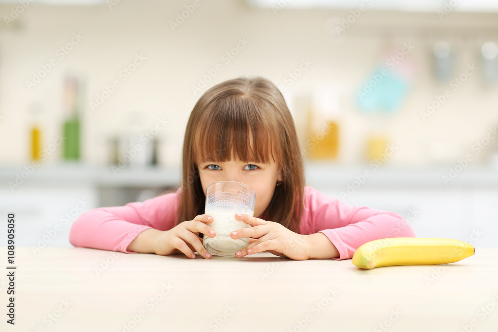 Beautiful little girl having breakfast with milk and banana in kitchen Beautiful little girl having breakfast with milk and banana in kitchen