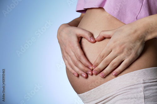 Pregnant woman making heart with her hands on blue background