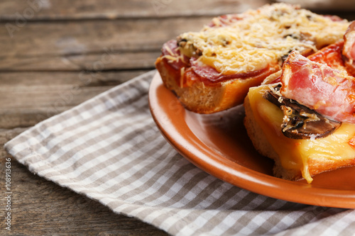 Hot pizza baguettes with bacon, salami and mushrooms on wooden table