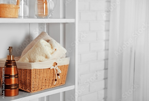 Bathroom set with towels, dispenser and basket on a shelf in light interior