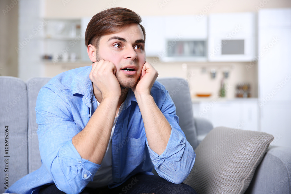 Young handsome man watching TV on a sofa at home Young handsome man watching TV on a sofa at home