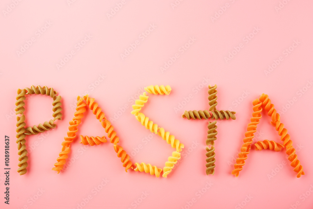 Pasta word made of varicolored fusilli on pink background