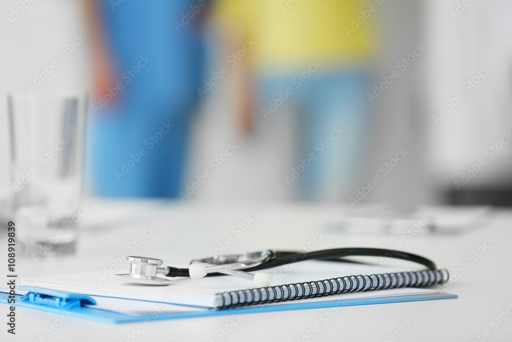 A notebook, a clipboard and a stethoscope on the doctor's table in the hospital, indoors A notebook, a clipboard and a stethoscope on the doctor's table in the hospital, indoors