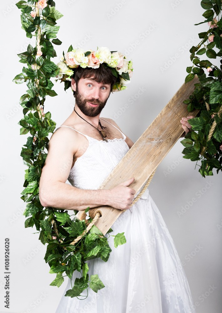 bearded man in a woman's wedding dress on her naked body, he holds the  swing. on
