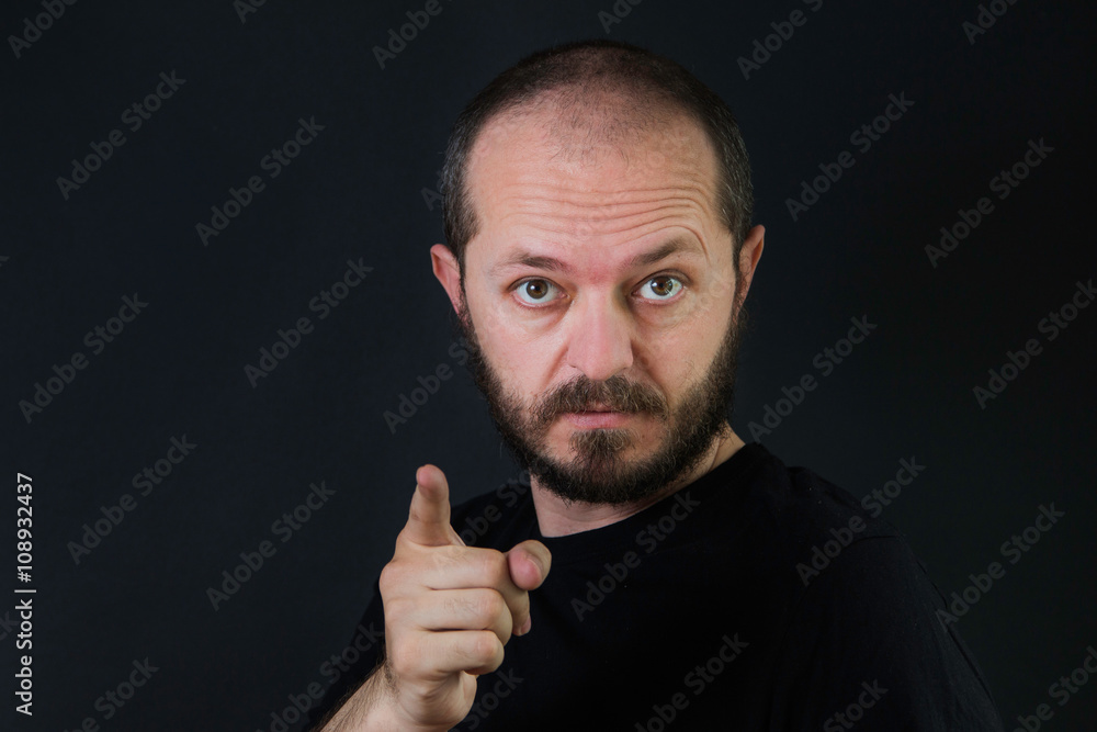 Serious man with beard and mustaches on black background in low key, pointing finger towards camera Serious man with beard and mustaches on black background in low key, pointing finger towards camera