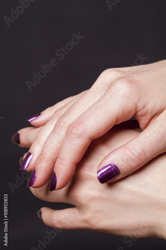 Close up of crossed over female hands decorated with purple fingernail paint over black
