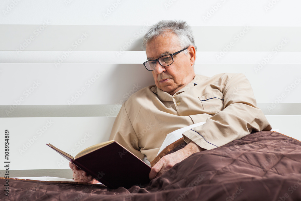 Senior man is lying in bed and reading a book before sleep Senior man is lying in bed and reading a book before sleep