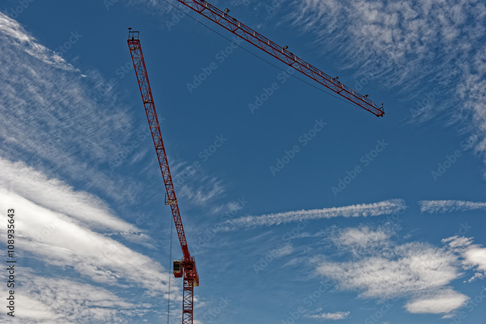 Tower crane painted red against the blue sky filled with clouds