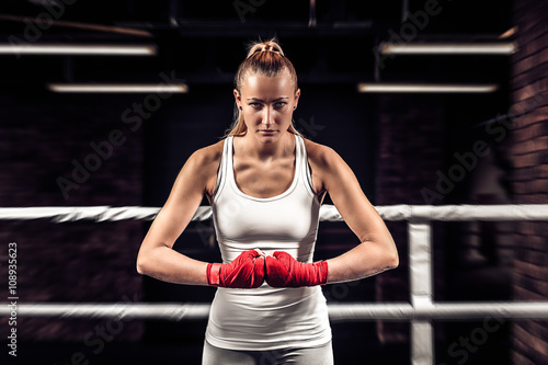 Young athlete girl boxer showing her fists with bandage ready for fight. Close up boxer female on uniform stands in the ring and getting ready to box.