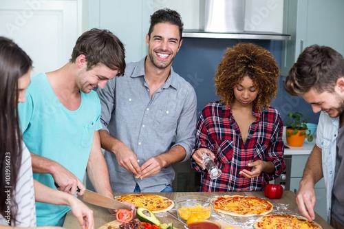 Cheerful young friends preparing pizza at home