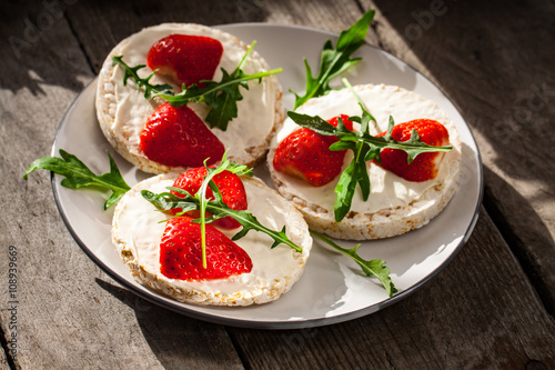 Multigrain rice cakes with strawberries fruit , soft mascarpone cheese and arugula for healthy breakfast.