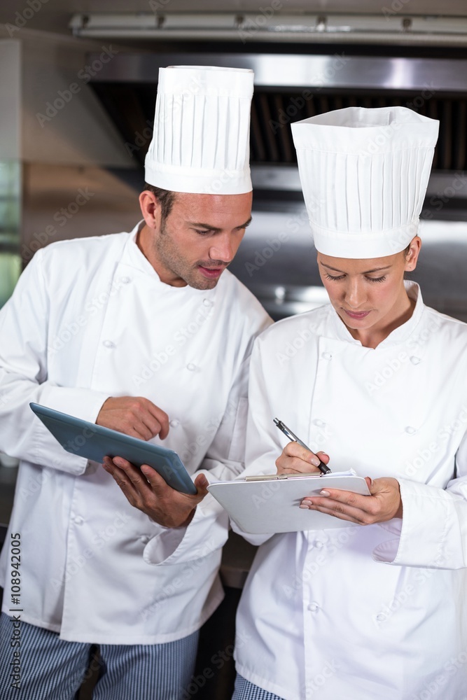 Focused chefs holding clipboards in kitchen