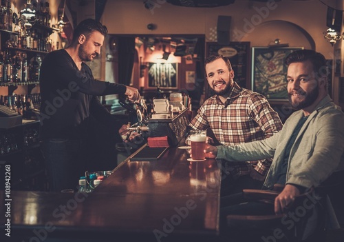 Cheerful old friends drinking draft beer at bar counter in pub.